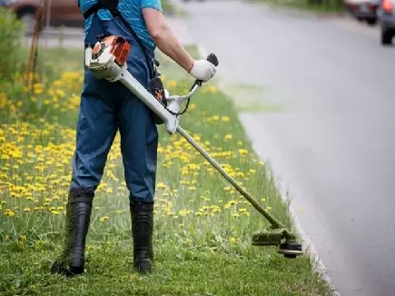 Image of a male landscape contractor weed eating where the road meets the property